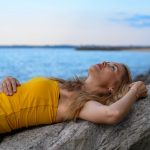 A woman peacefully relaxes on rocks by the sea in Tallinn during a calm summer day.