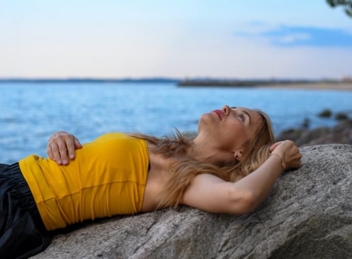 A woman peacefully relaxes on rocks by the sea in Tallinn during a calm summer day.